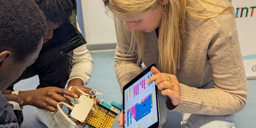 Eine Frau und zwei Jugendliche programmieren gemeinsam einen kleinen Roboter mithilfe eines Tablets.