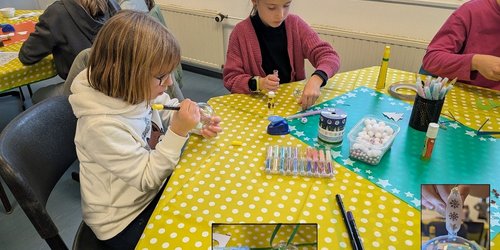 Zwei Mädchen sitzen an einem Basteltisch und gestalten mit Stiften und Materialien eine leuchtende Weihnachtskugel.